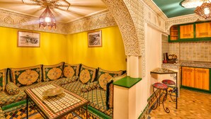 A room with a green sofa, a small table, and a kitchen area with wooden cabinets and a tiled backsplash. - Dar ayour appartements (Essaouira)