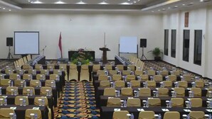 A conference room with rows of tables and chairs, a podium, and two screens. - Hotel Sentral Jakarta (Jakarta)
