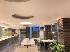 A modern hotel lobby with a reception desk, seating area, and a TV screen.