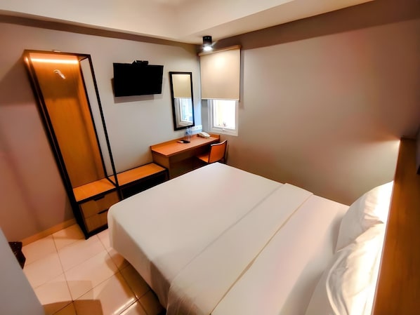 A hotel room with a bed, a desk, a chair, a mirror, a TV, and a window.