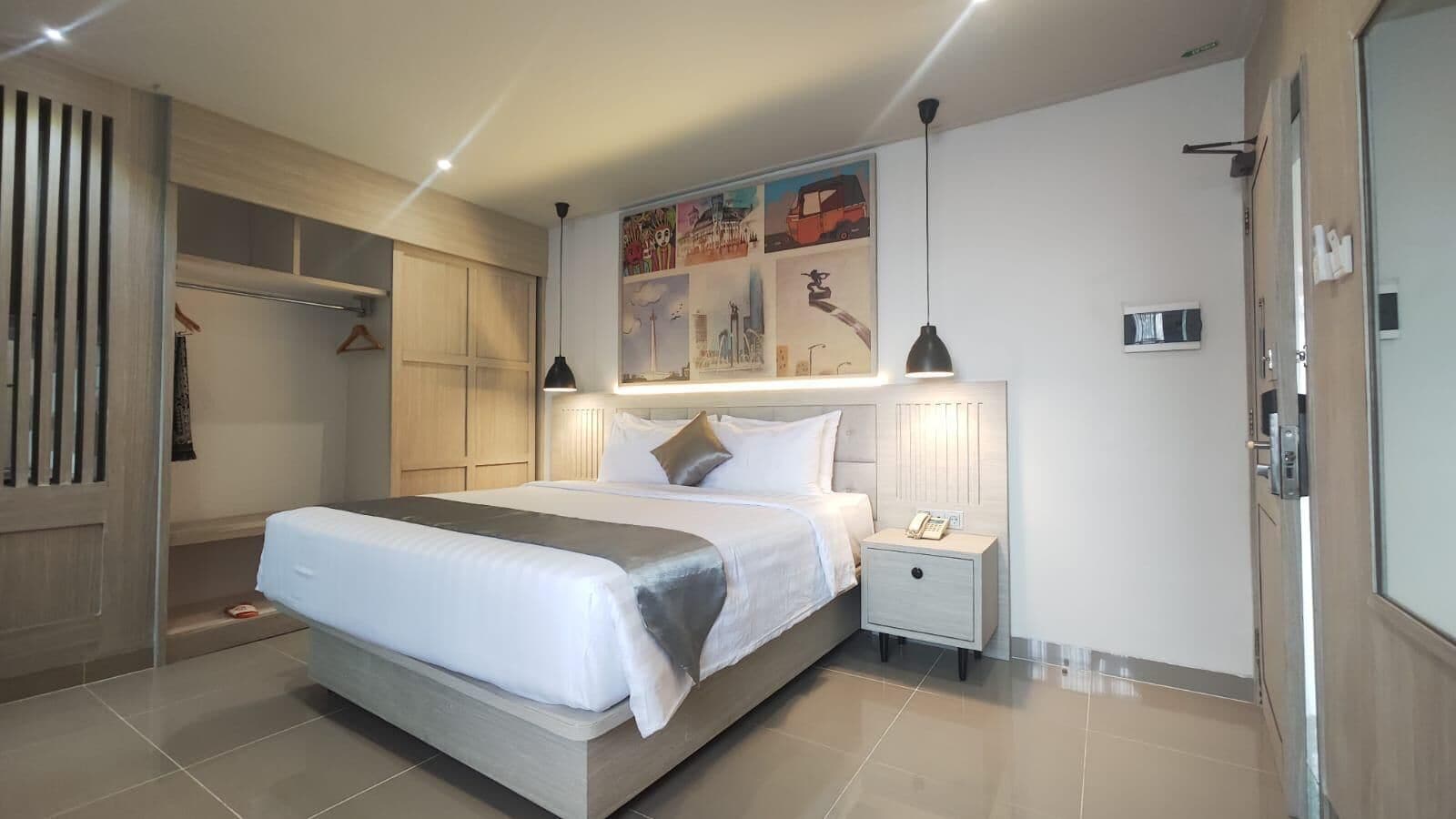 A modern hotel room with a large bed, bedside tables, a wardrobe, and a painting on the wall.