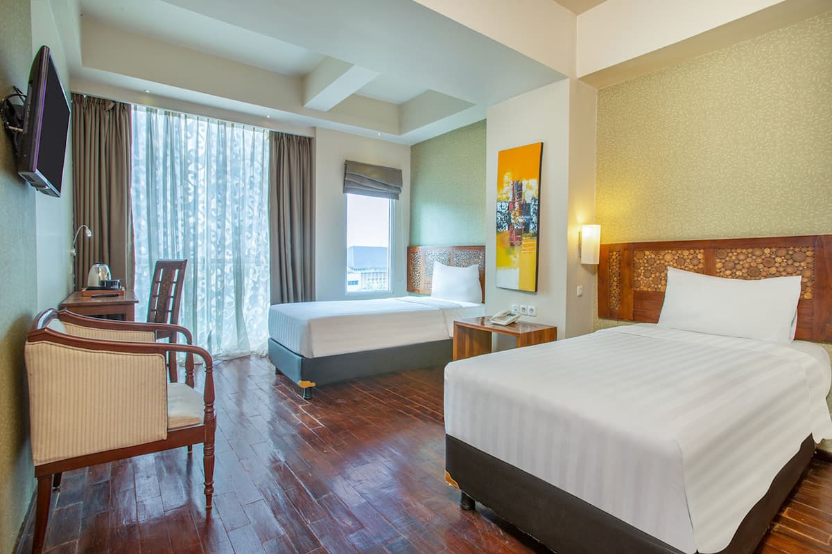 Ein Hotelzimmer mit zwei Betten, einem Schreibtisch mit Stuhl, einem Fernseher und einem großen Fenster mit Vorhängen.