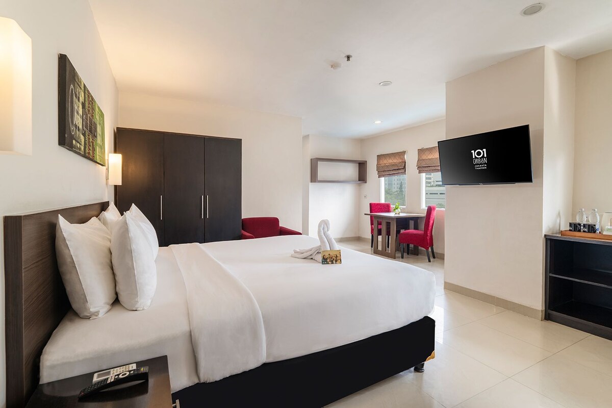 Una habitación de hotel con cama, escritorio, televisor y zona de comedor con sillas.