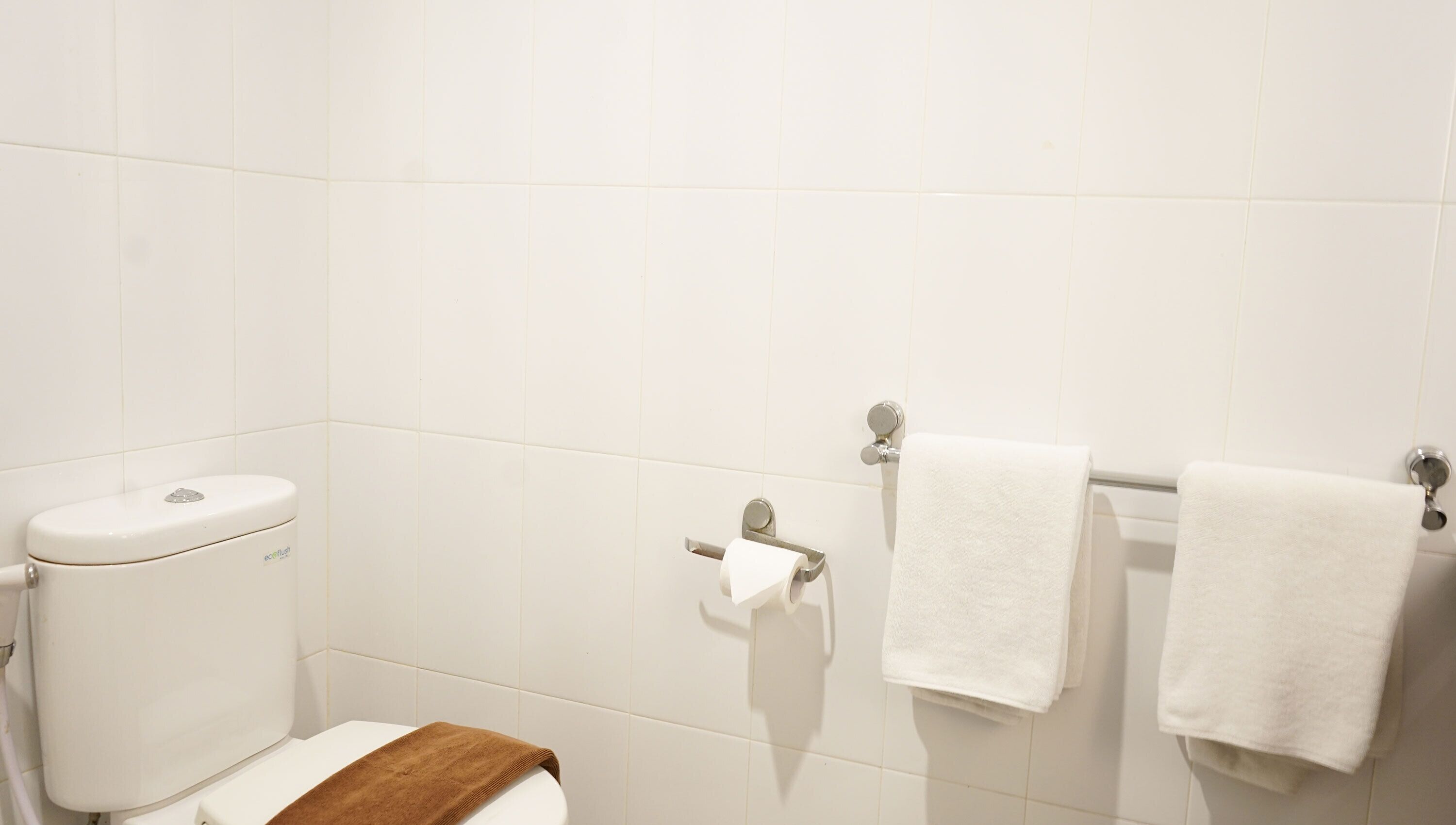 Un baño con un inodoro, un perchero con dos toallas blancas y un dispensador de toallas de papel.