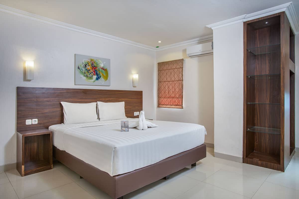 Ein modernes Hotelzimmer mit einem großen Bett, einem Holzkopfende, einem Nachttisch, einer wandmontierten Lampe, einem Fenster mit Jalousien und einem Holzschrank.