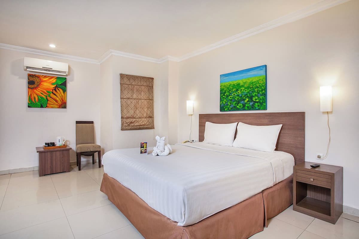 Ein Hotelzimmer mit einem großen Bett, einem Sessel, einem Nachttisch, einer Klimaanlage und zwei an der Wand befestigten Bildern.