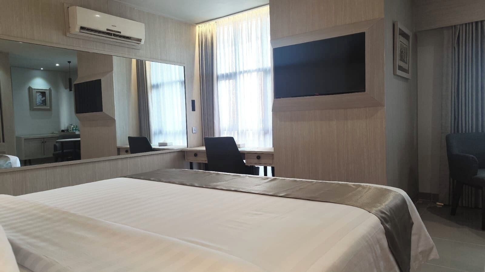 A hotel room with a large bed, a desk, a chair, a flat-screen TV, and a large mirror.