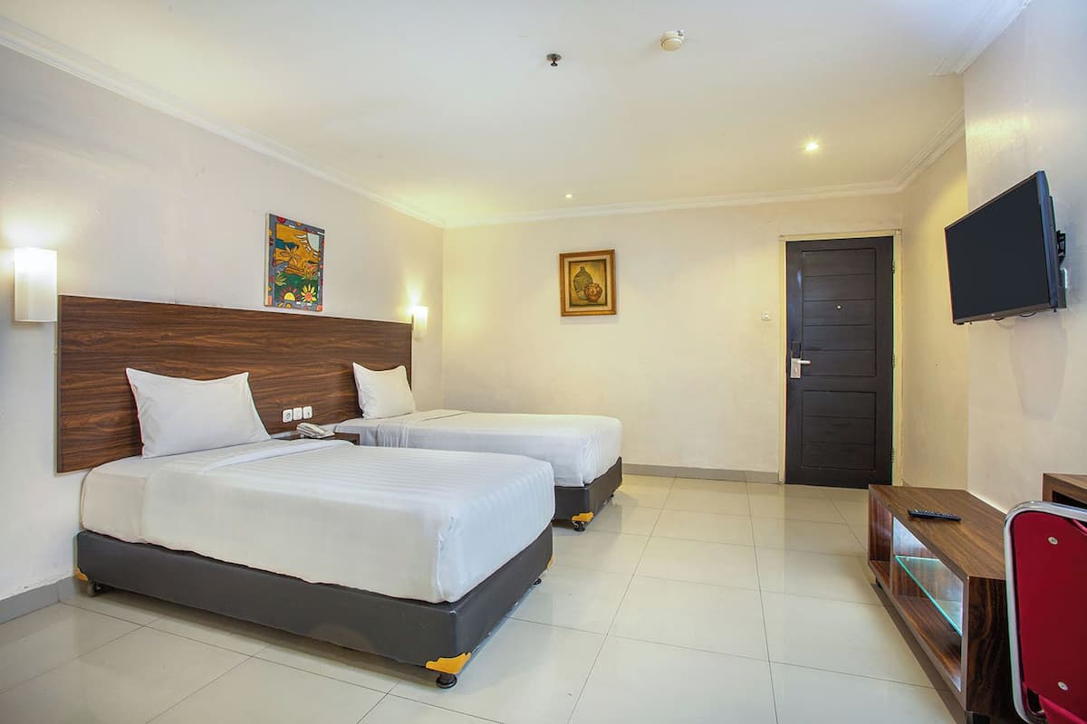 A hotel room with two beds, a desk with a TV, and a door.