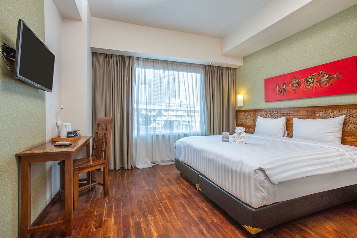 Ein Hotelzimmer mit Bett, Schreibtisch, Sessel, Fernseher und einem Fenster mit Vorhängen.