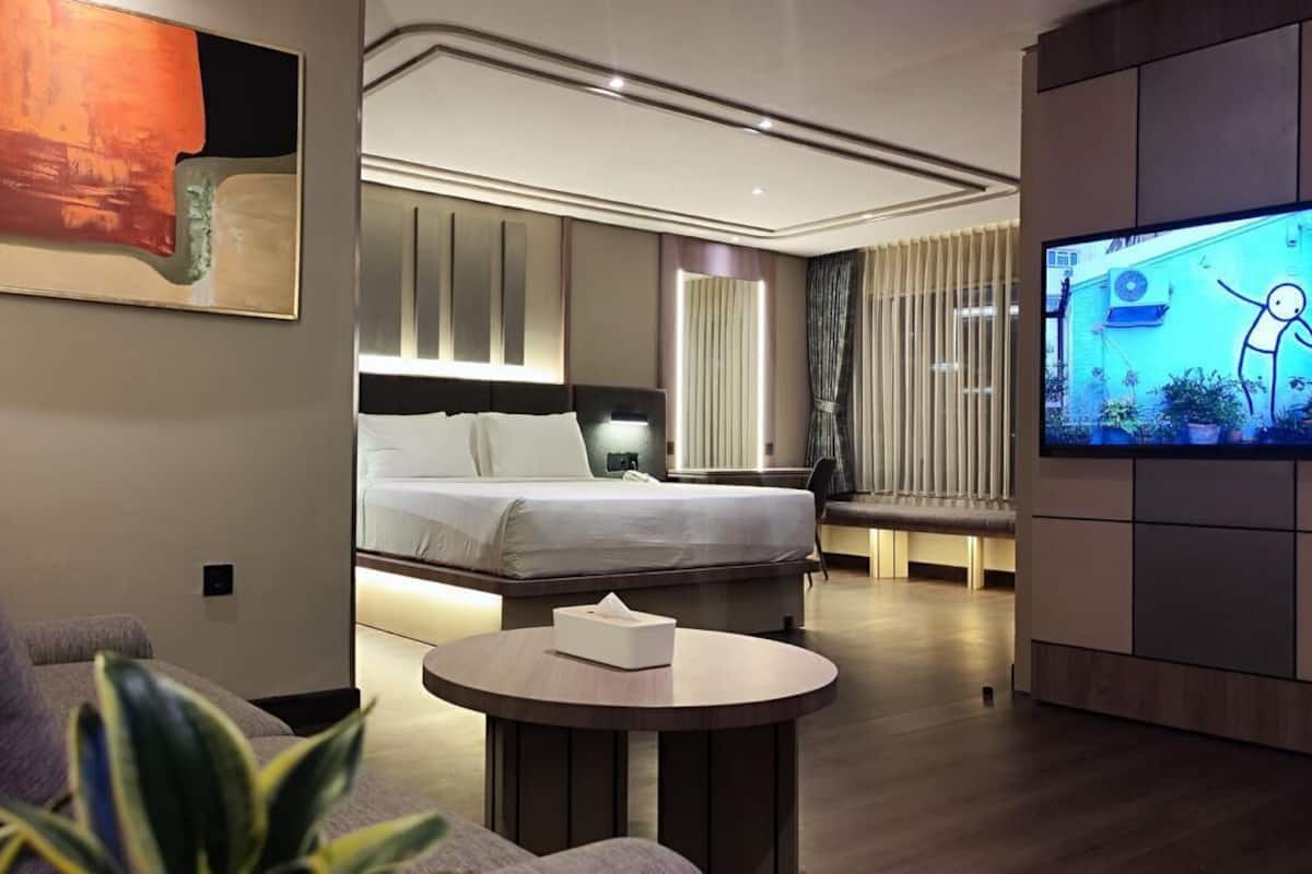 Ein modernes Hotelzimmer mit einem großen Bett, einem runden Couchtisch, einem Fernseher und einem Bild an der Wand.
