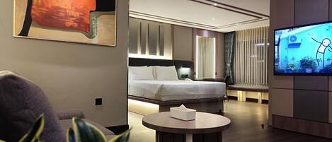 Una habitación de hotel moderna con una cama grande, una mesa redonda para café, un televisor y un cuadro en la pared.