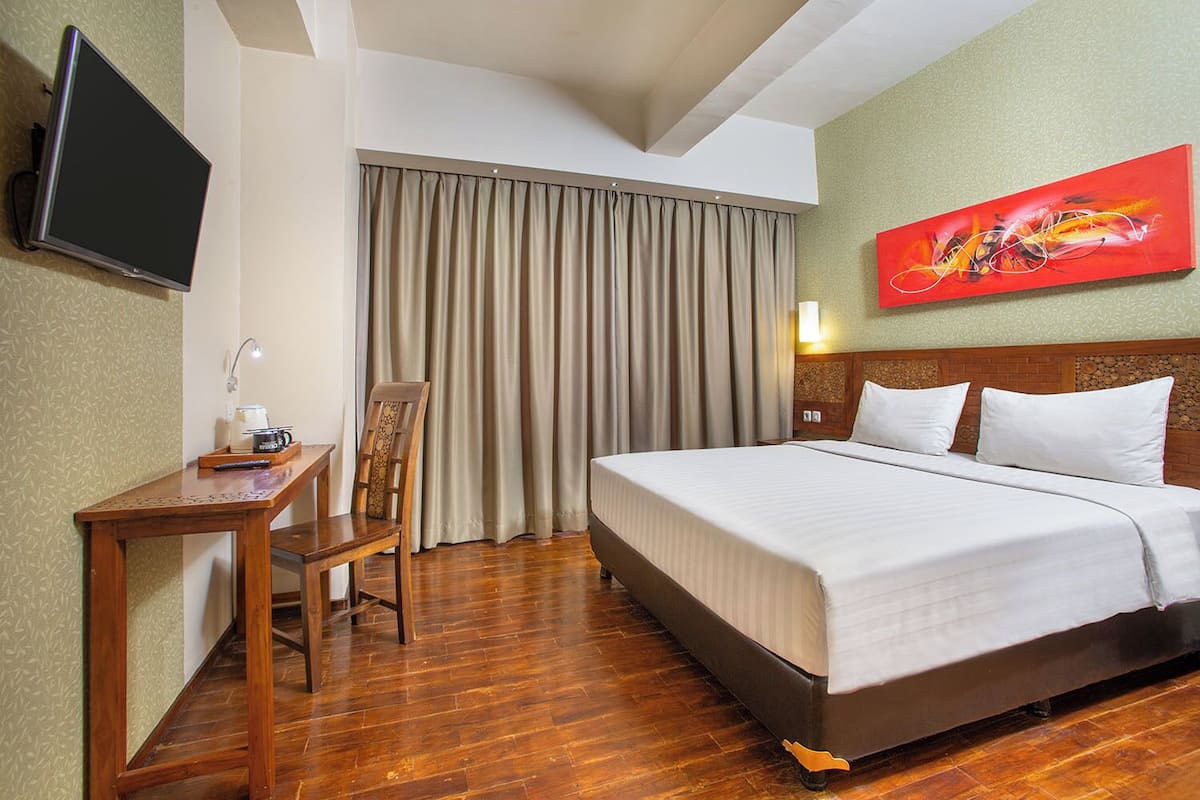 Ein Hotelzimmer mit Bett, Schreibtisch, Stuhl, Fernseher und einem Bild an der Wand.
