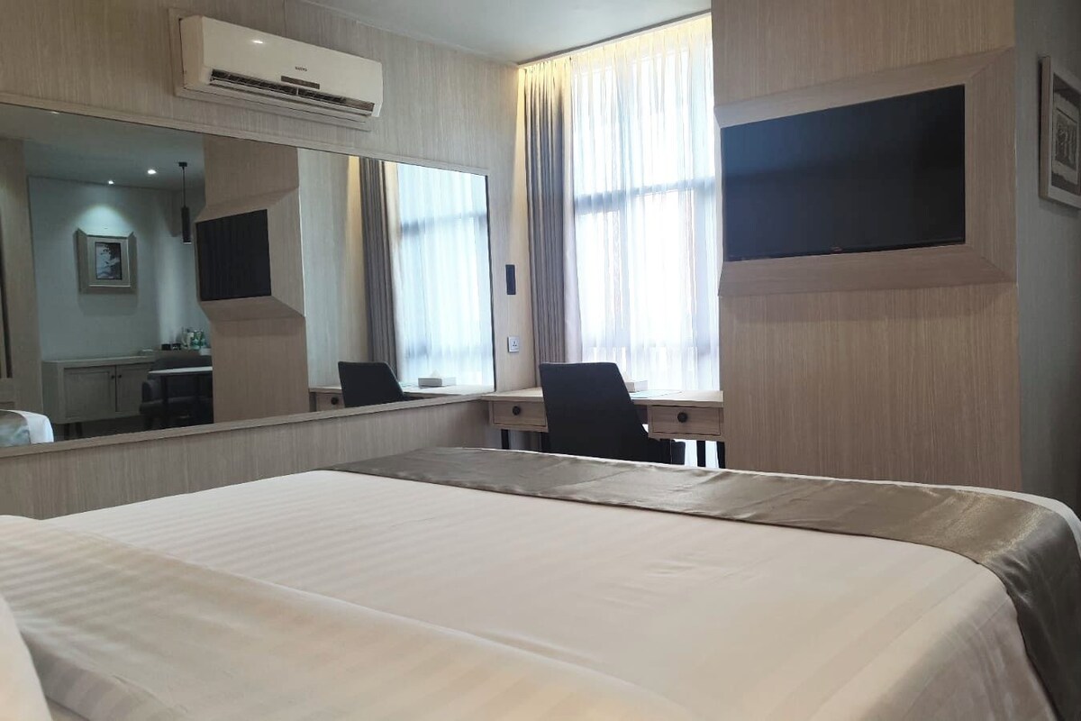 Ein Hotelzimmer mit einem großen Bett, einem Schreibtisch, einem Sessel, einem Flachbildfernseher und einem großen Spiegel.