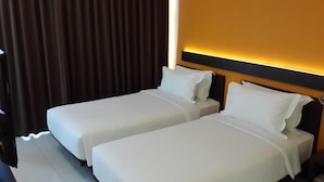 A hotel room with two single beds, a dark curtain, and a wall-mounted light fixture. - V Hotel Tebet, Jakarta (Jakarta)