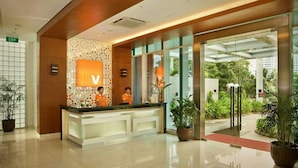 A hotel reception area with a modern design, featuring a reception desk, a large illuminated 'V' sign, and glass doors leading outside. - V Hotel Tebet, Jakarta (Jakarta)