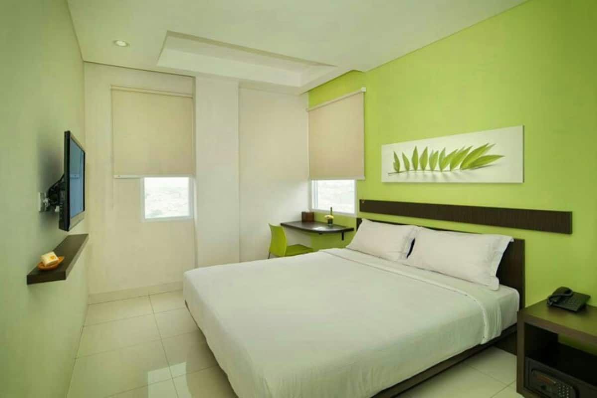 Una habitación de hotel con cama, escritorio, silla, televisor y un cuadro en la pared.