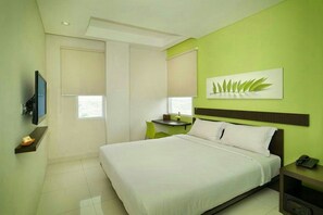 Quarto de hotel com cama, escrivaninha, cadeira, televisão e um quadro na parede.