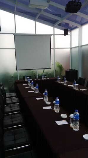 Uma sala de conferência com uma mesa comprida, cadeiras, uma tela de projetor e garrafas de água.