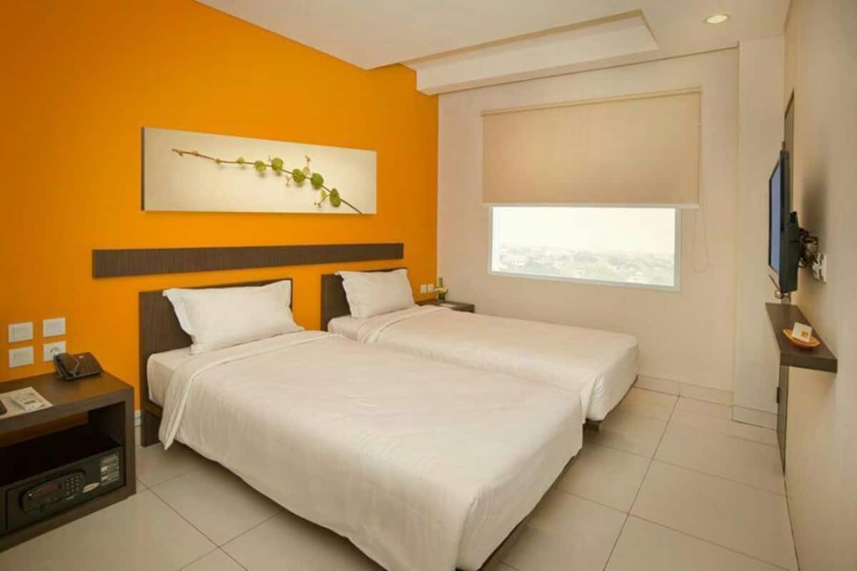 Habitación de hotel con dos camas, un ventanal grande, un televisor de pantalla plana y una mesita de noche con un teléfono y una lámpara.