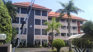 A multi-story building with a red-tiled roof, surrounded by palm trees and a covered seating area. - Jepara Indah Hotel (Jepara)