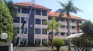 A multi-story building with a red-tiled roof, surrounded by palm trees and a covered seating area. - Jepara Indah Hotel (Jepara)