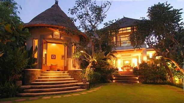 A bungalow with a thatched roof and a second-story balcony, surrounded by lush greenery. - The Graha Cakra (MALANG)