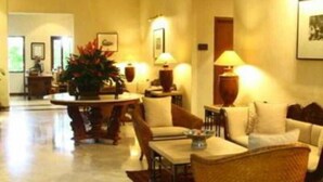 A spacious hotel lobby with a round dining table, several chairs, a sofa, and a large potted plant. - The Graha Cakra (MALANG)