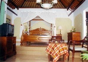 A room with a bed, a television, a table with a checkered tablecloth, and a chair. - The Graha Cakra (MALANG)