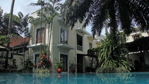 A modern building with a swimming pool, surrounded by lush greenery and palm trees. - The Graha Cakra (MALANG)