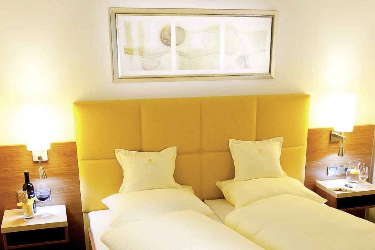 Une chambre d’hôtel avec un lit double, deux tables de chevet, un tableau encadré au mur et une fenêtre avec des rideaux.