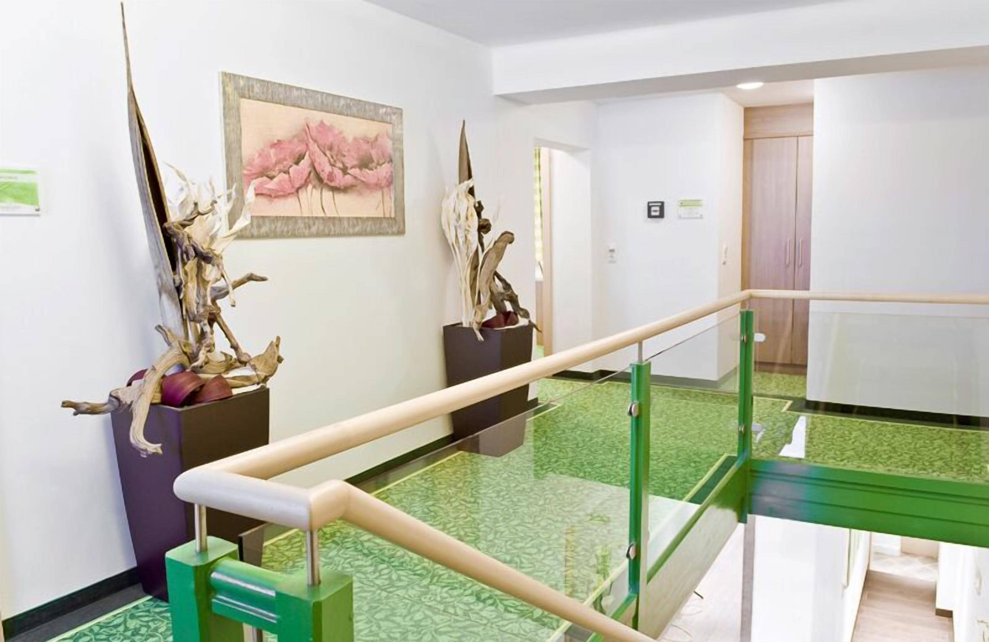 Un hall d’hôtel avec une moquette verte, une rambarde en verre et deux sculptures posées sur des piédestaux.