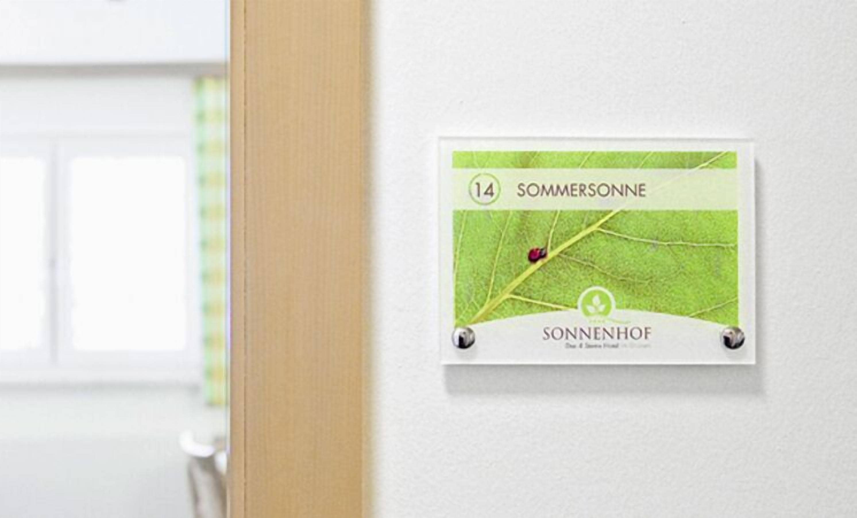 Une enseigne fixée au mur, ornée d’une feuille verte et d’une coccinelle, et portant les inscriptions « SOMMERSONNE » et « SONNENHOF ».