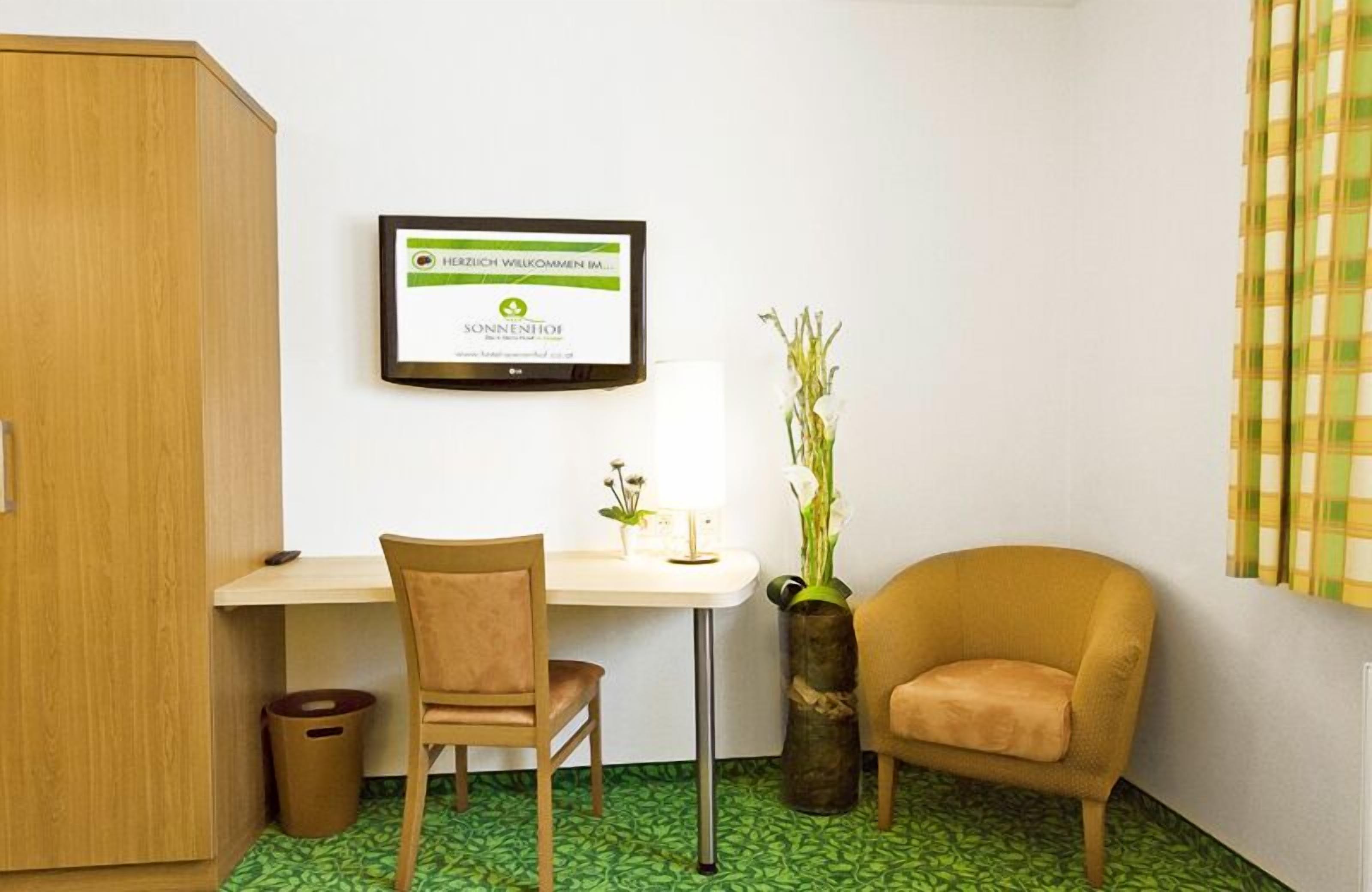 A small room with a desk, a chair, a sofa, a trash bin, and a framed sign on the wall.
