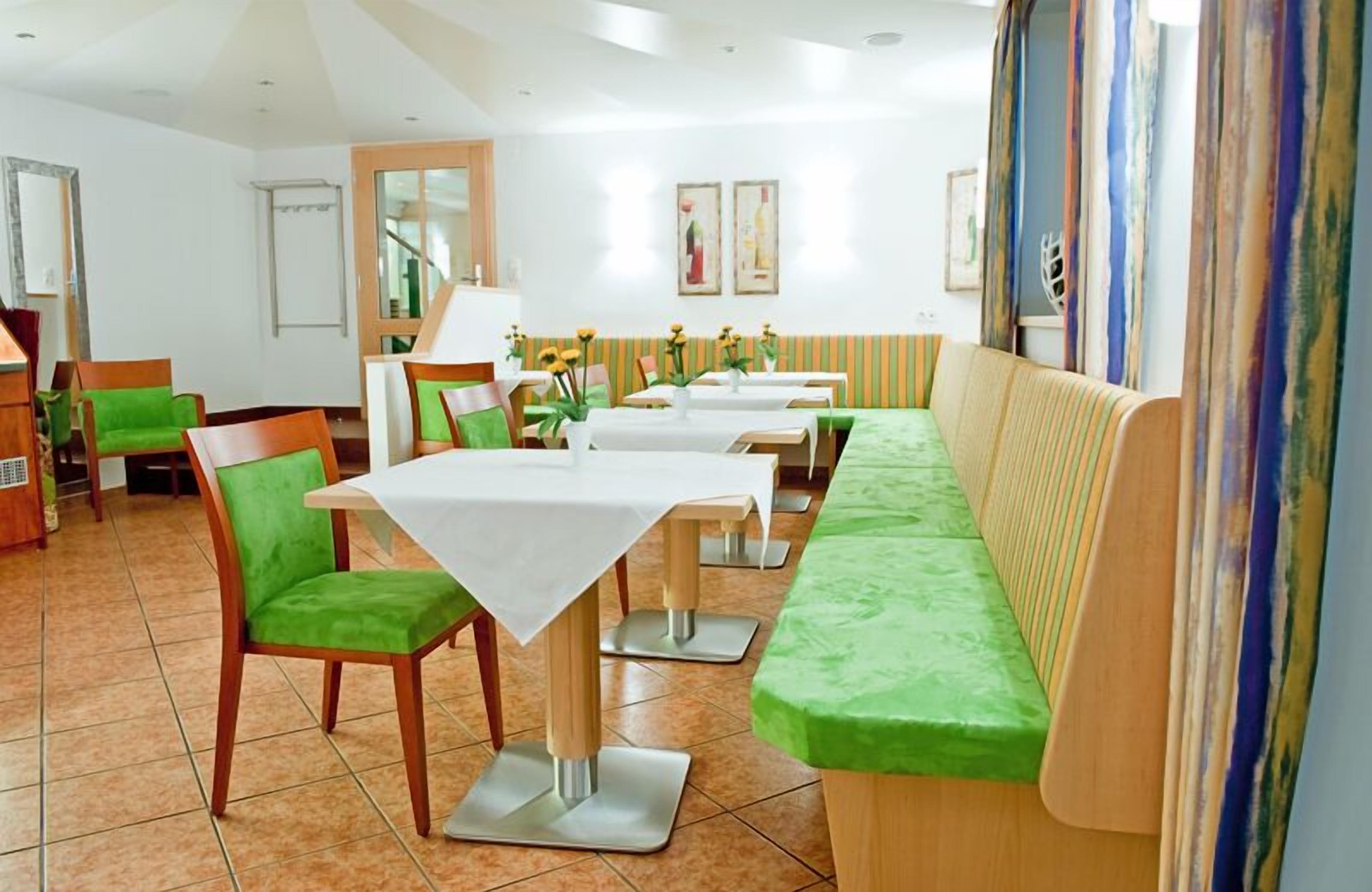 A dining area with green cushioned chairs and tables, a wooden bench, and a striped curtain.