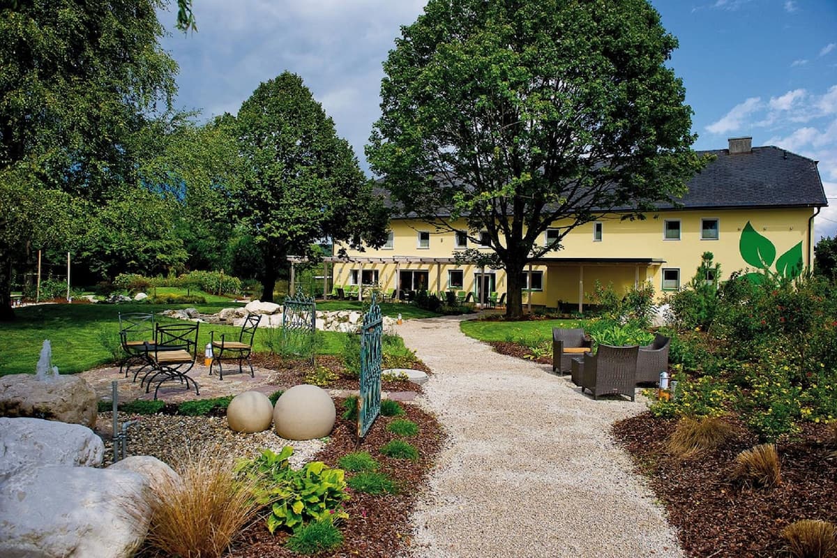 Un bâtiment jaune avec un jardin et un chemin menant à un espace extérieur aménagé pour s’asseoir.