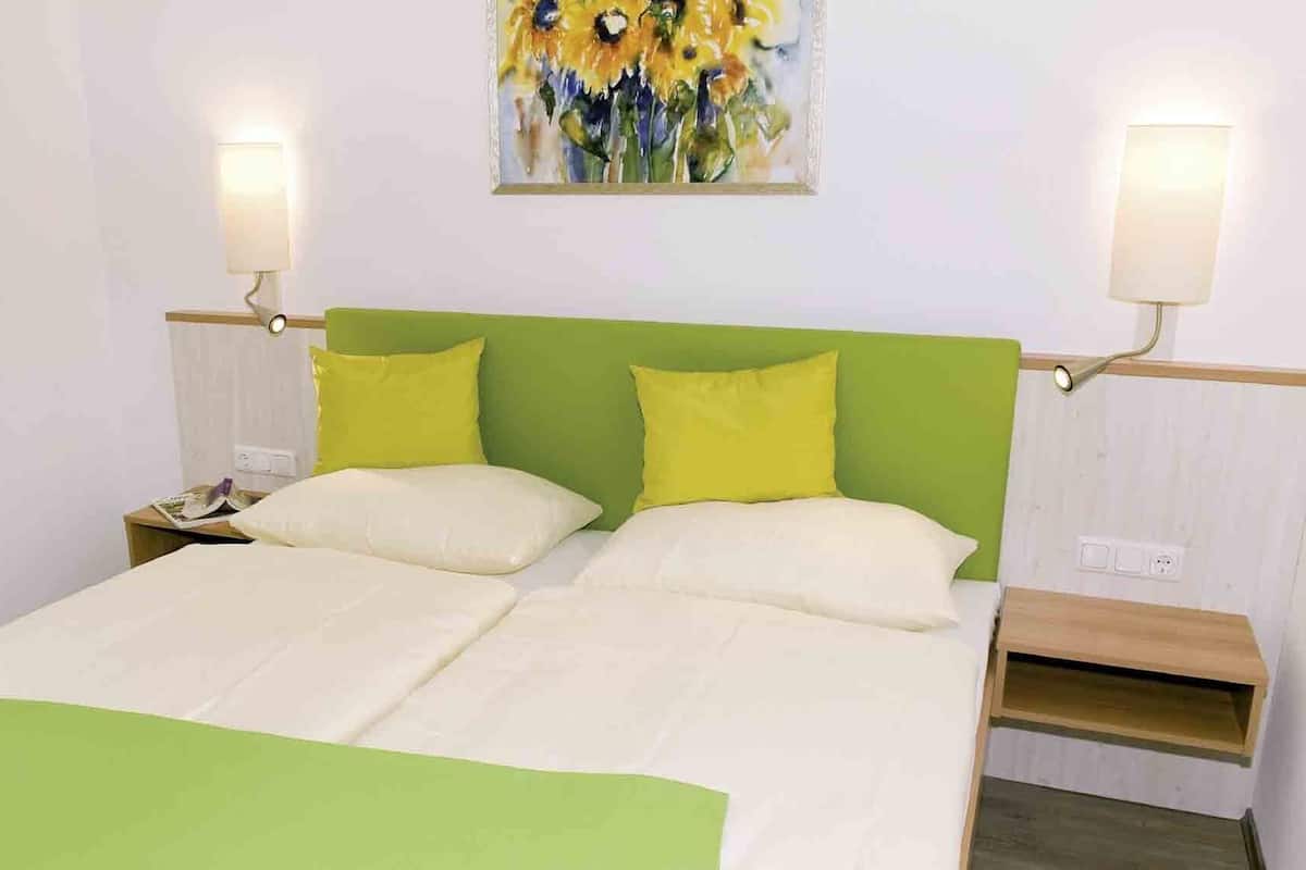 Un lit double avec une tête de lit verte et deux oreillers, une table de chevet avec une lampe et un tableau au mur.