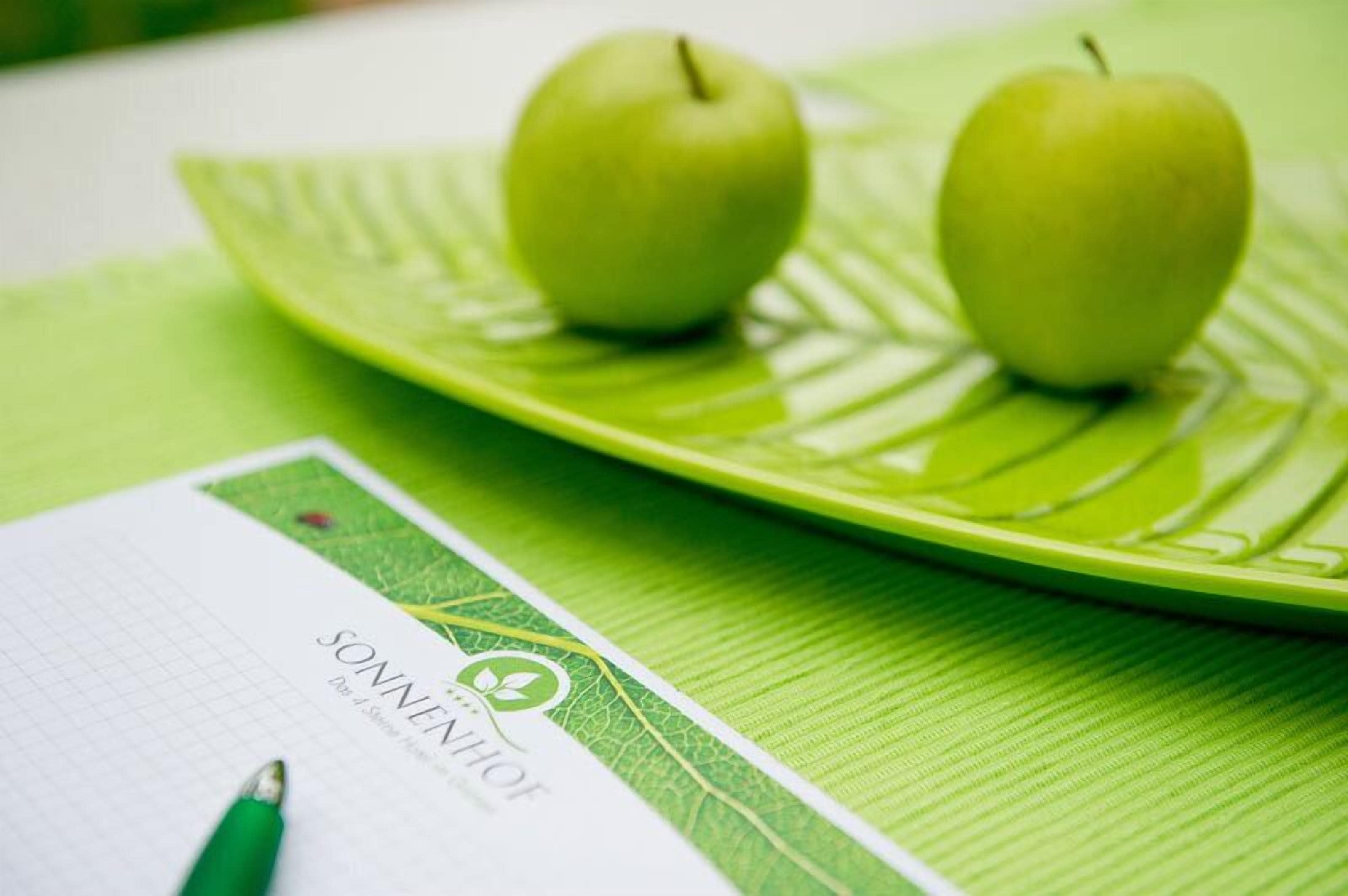 A green leaf-shaped plate with two green apples and a notebook with a pen on it.
