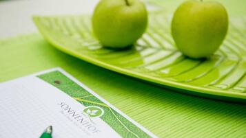 A green leaf-shaped plate with two green apples and a notebook with a pen on it.
