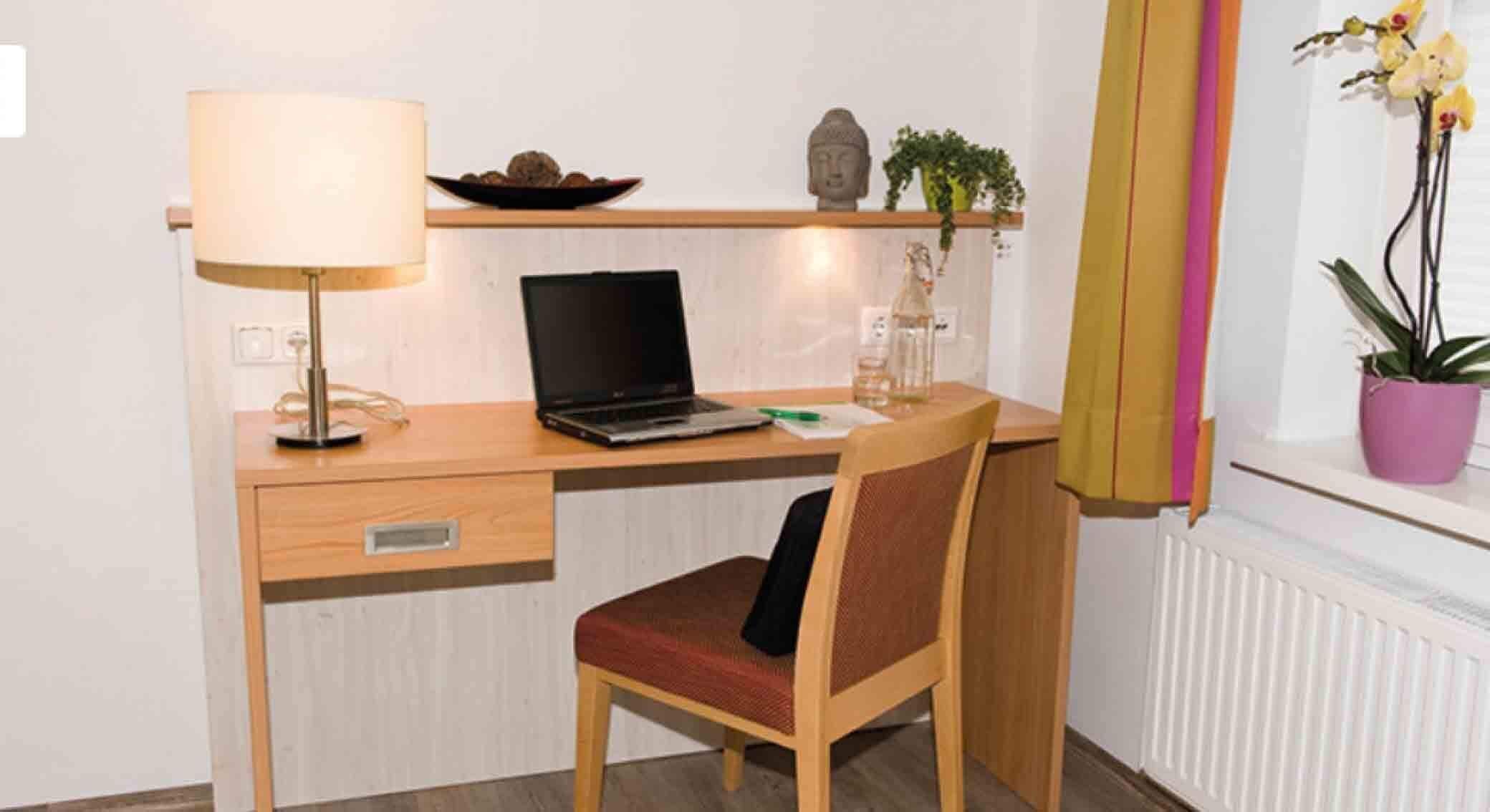 Una scrivania in legno con un portatile, una lampada e una sedia.