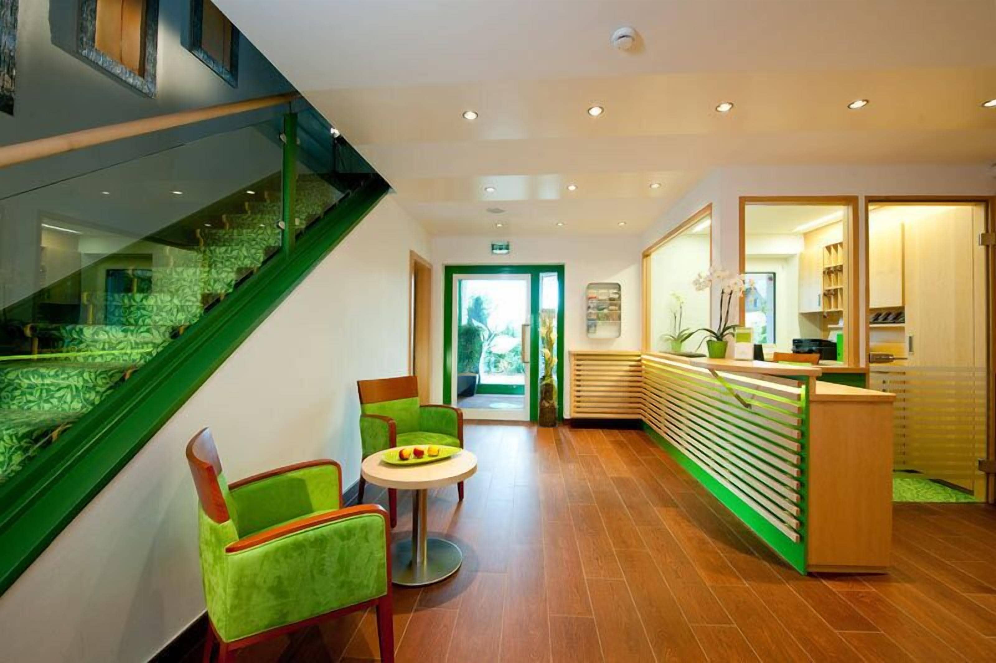 A modern hotel lobby with a staircase, seating area, reception desk, and a view of the outdoors.