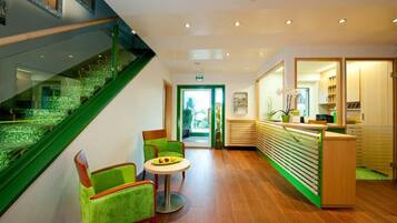A modern hotel lobby with a staircase, seating area, reception desk, and a view of the outdoors.
