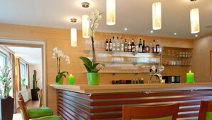 Zona de bar con sillas de madera, barra y una variedad de botellas y vasos.