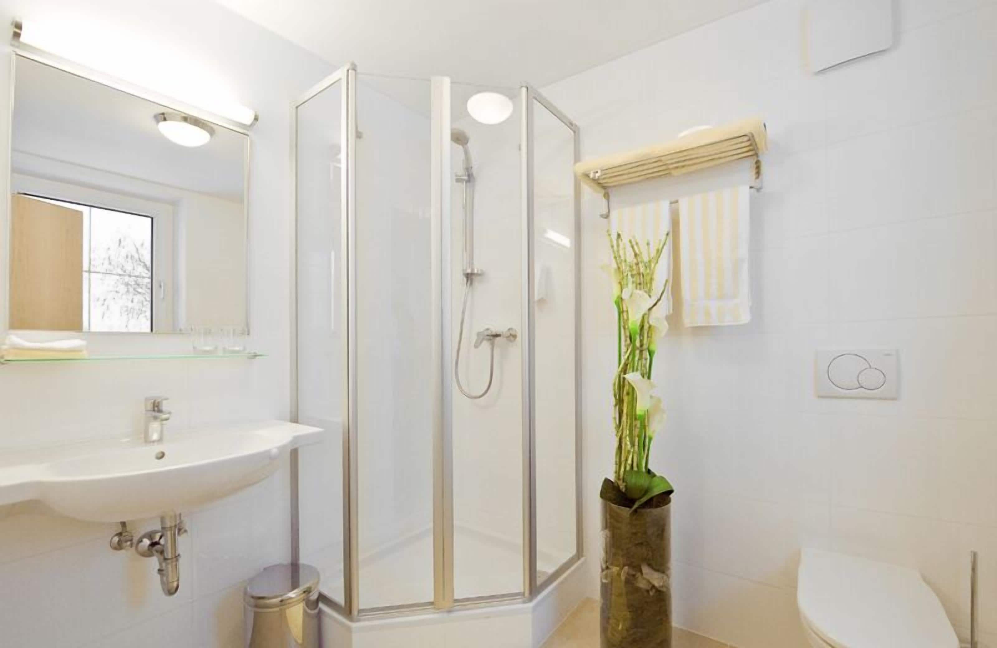 Un baño moderno con ducha envuelta en vidrio, un lavabo, un inodoro y un florero con flores.