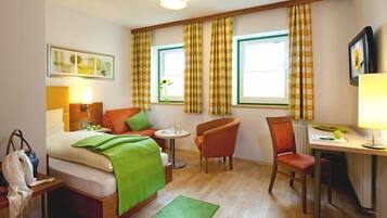 A hotel room with a bed, a desk, two chairs, a table, a green rug, and curtains.