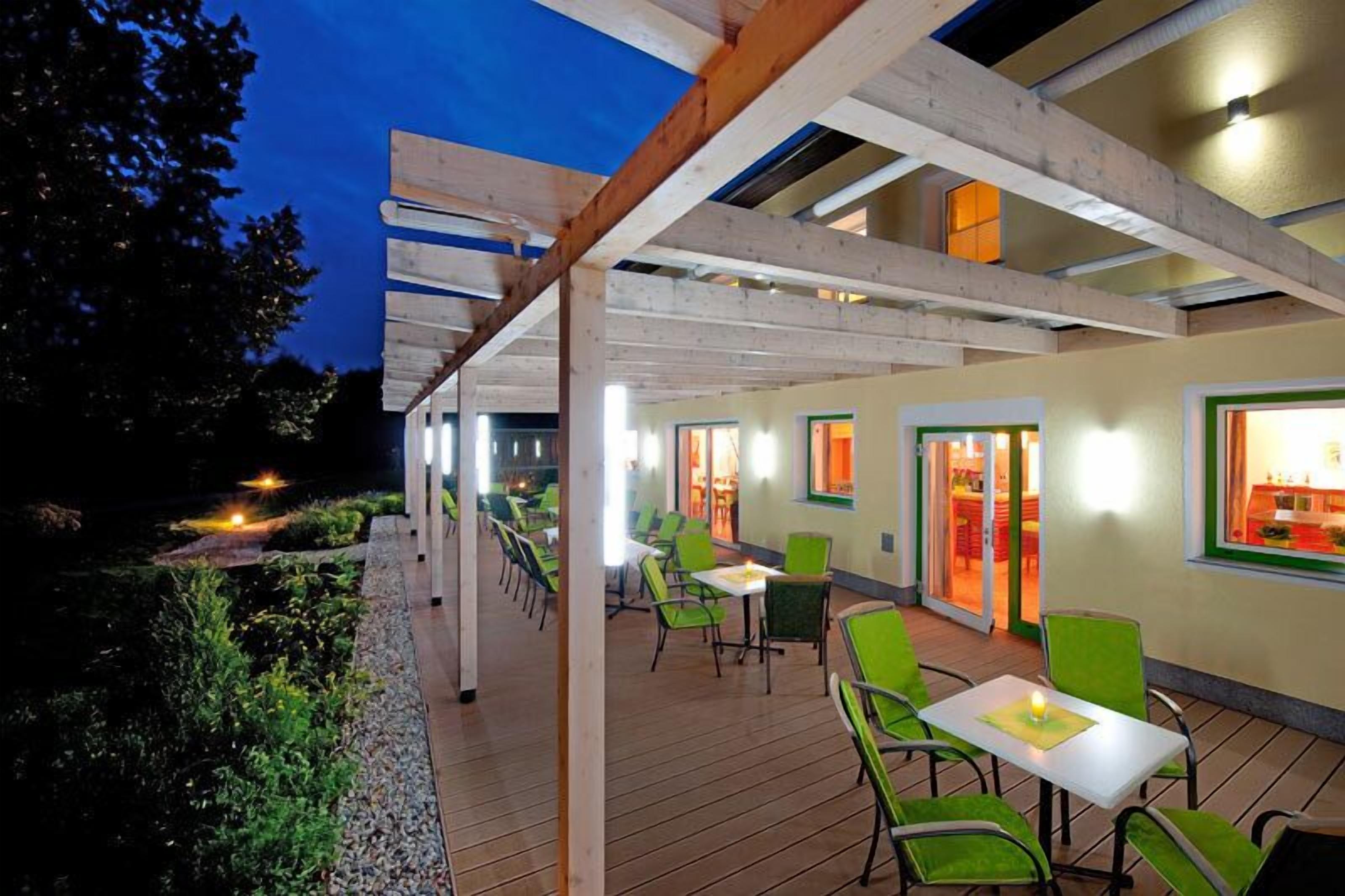 Area patio esterna con travi in legno e sedie verdi.