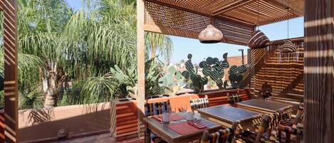 An outdoor dining area with wooden furniture and a view of tropical plants.