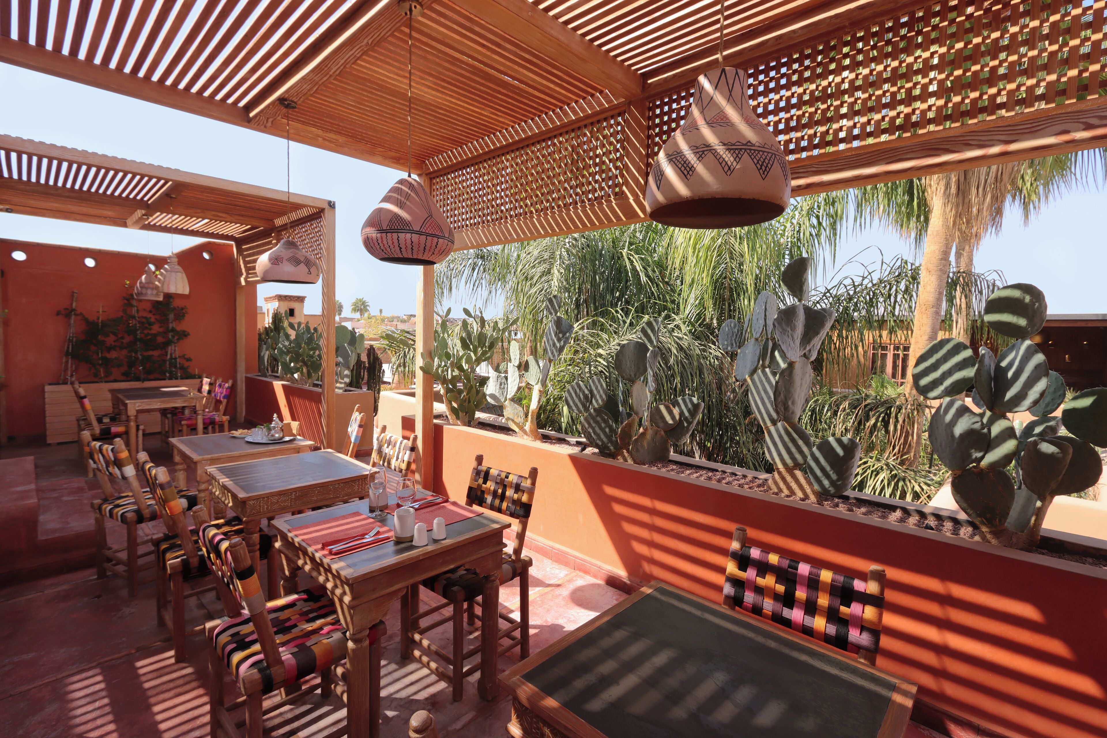 An outdoor dining area with wooden tables and chairs, a patterned bench, and hanging pottery lamps.