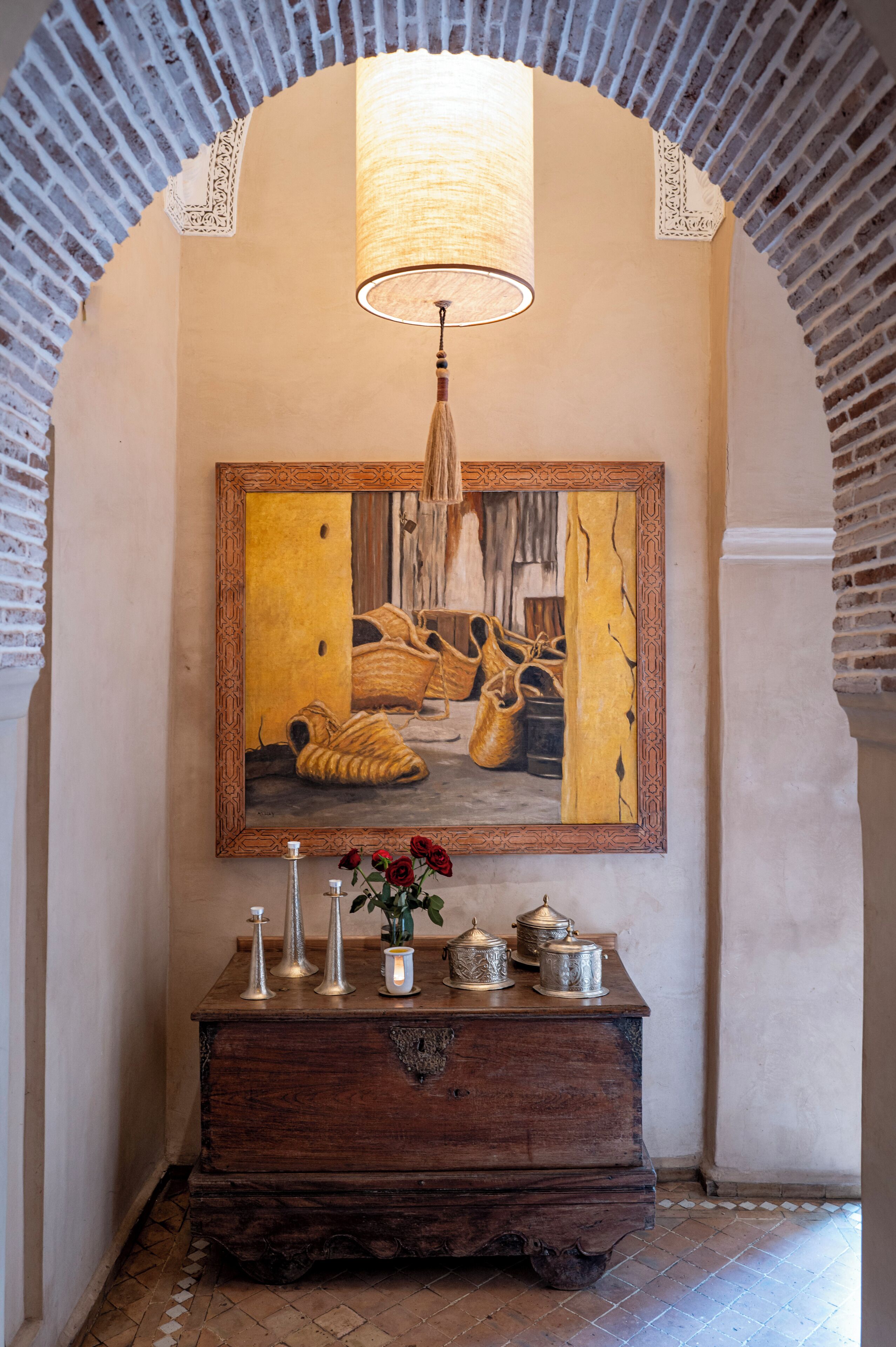 A hallway with a wooden dresser, a framed painting of shoes, and a hanging lamp.