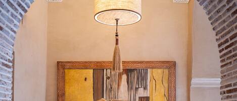 A hallway with a wooden dresser, a framed painting of shoes, and a hanging lamp.