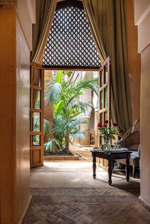 Un couloir avec une porte en bois donnant sur un jardin, une table ornée d’un vase de fleurs et une chaise.